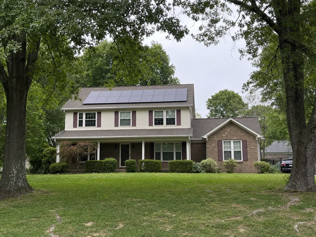 A rooftop solar array on the asphalt shingle roof of a two storey house in a Middle Tennessee neighbourhood, with mature hardwoods either side